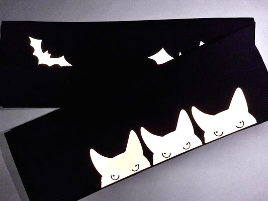 May include: Three white cats peeking out from behind a black fabric with a white bat silhouette on top.